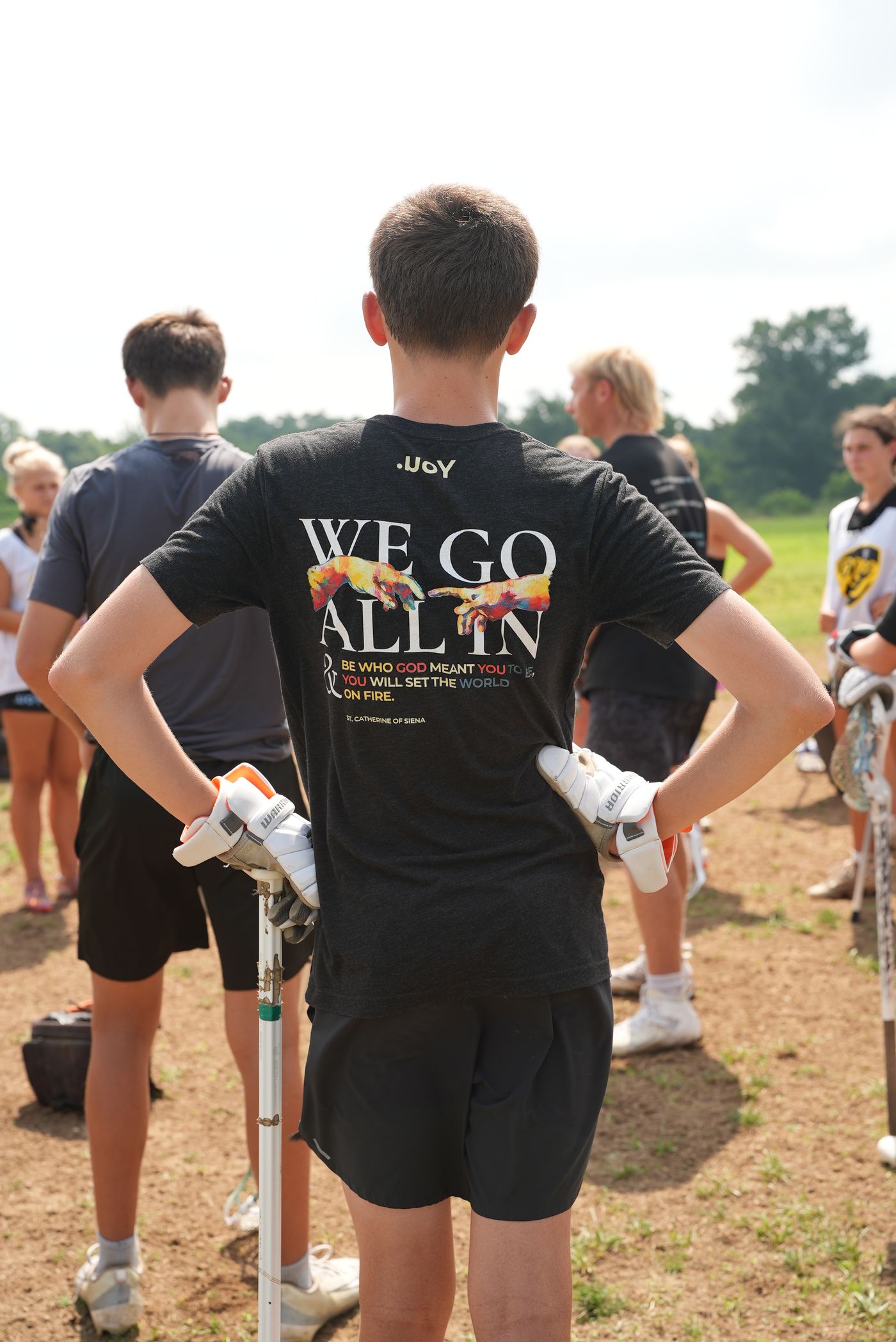 An athlete in a WE GO ALL IN shirt, hands on hips, watching the field.